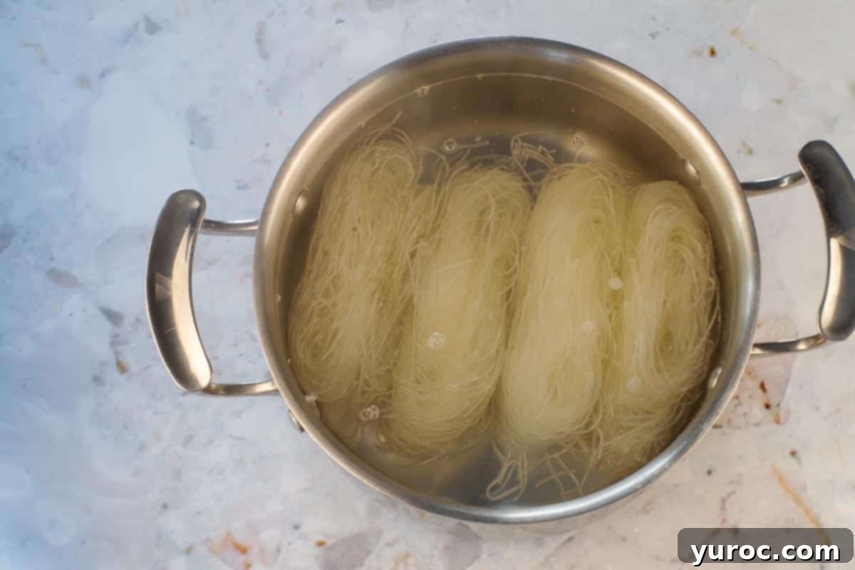 Vermicelli noodles soaking in hot water in a medium pot, preparing for the Thai chicken noodle salad.