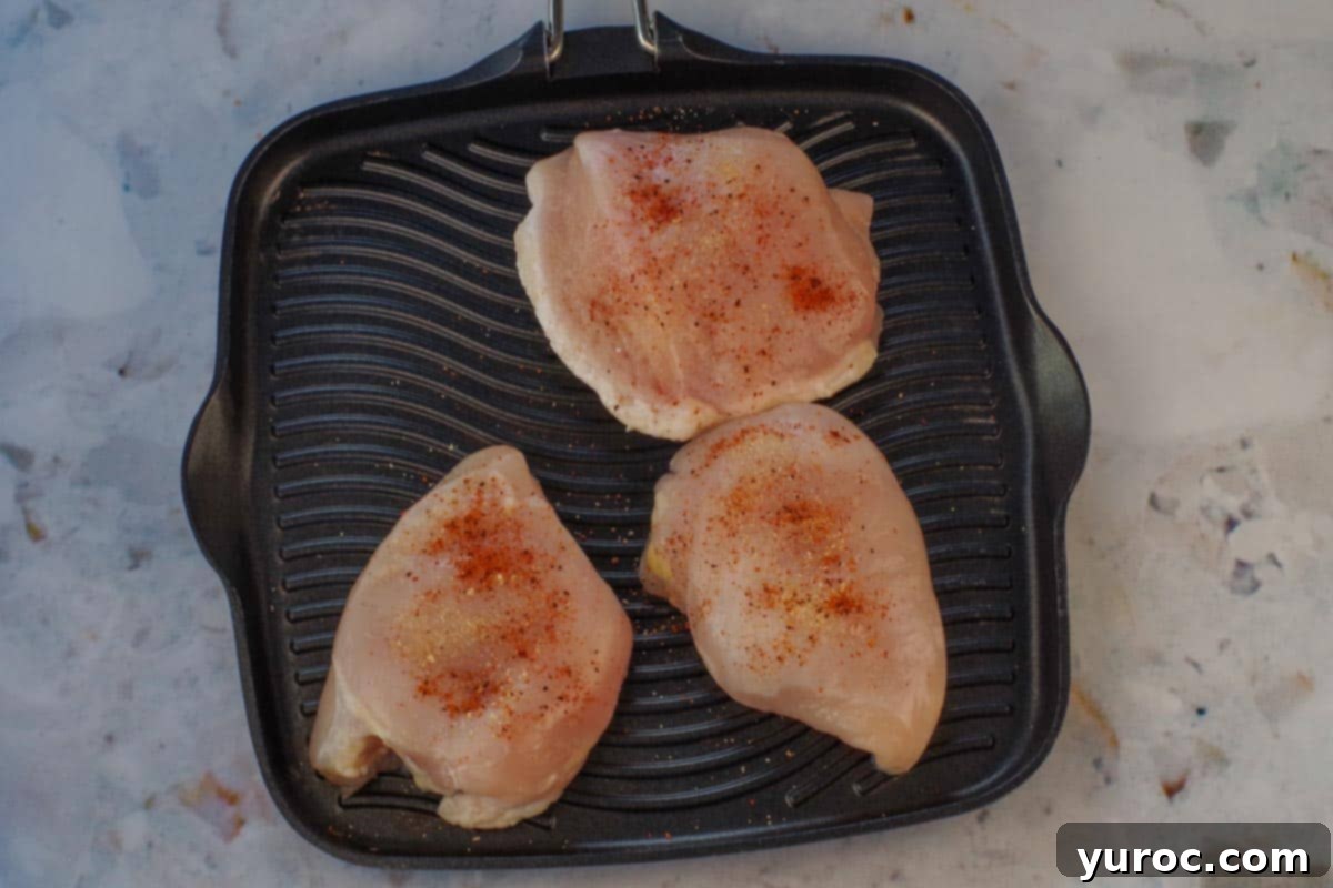 Three raw, seasoned chicken breasts placed on an indoor stovetop grill, ready for cooking.