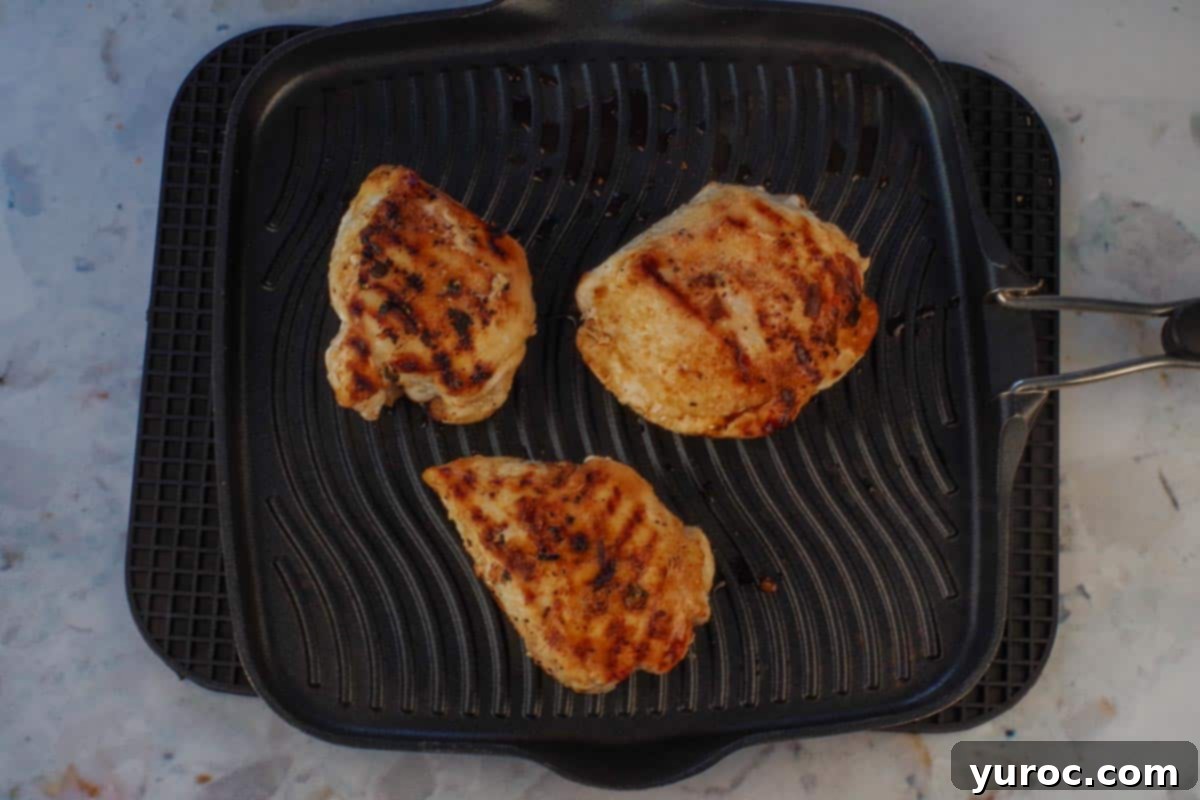 Three cooked chicken breasts resting on a stovetop grill, showing perfect grill marks.