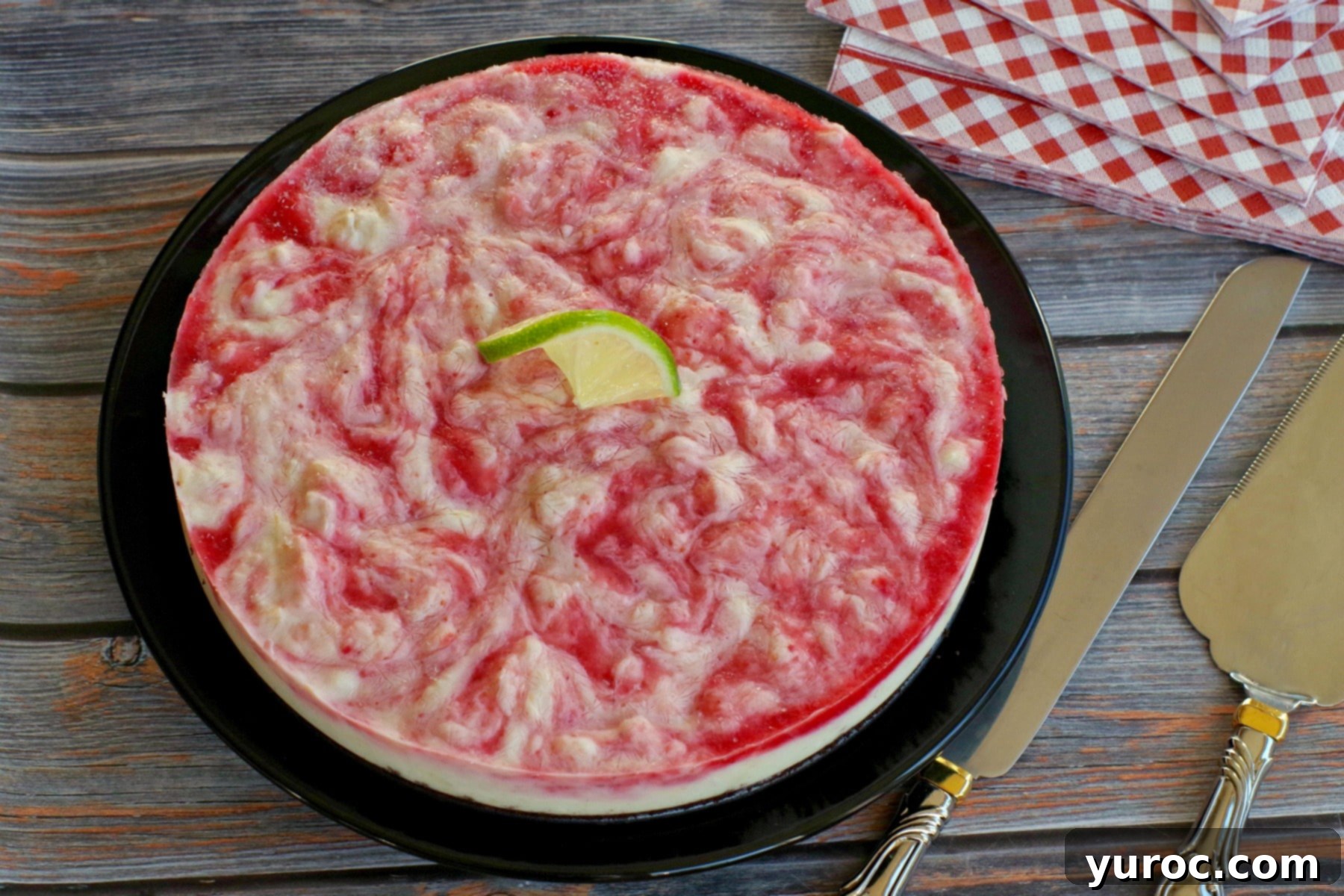 A vibrant slice of Miami Vice Frozen Cheesecake showcasing its red and white layers, garnished with a lime wedge.