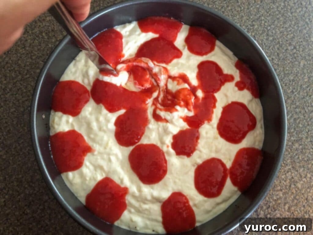 A butter knife gently swirling the red strawberry mixture into the white pina colada layer, creating a beautiful marbled effect.