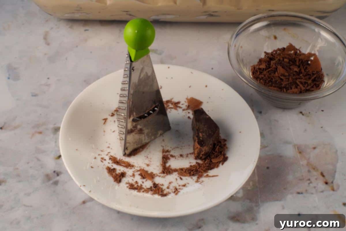 Decadent Dulce De Leche Chocolate Raspberry Icebox Cake 14 Mini grater on a white plate grating chocolate for garnish.