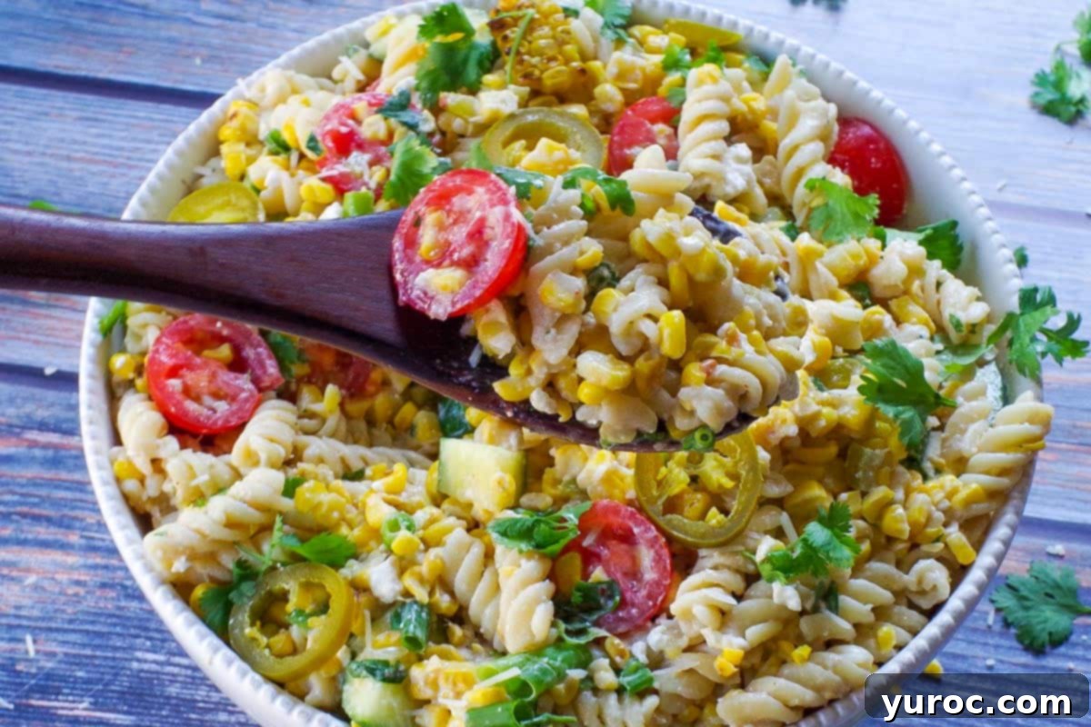 Decadent Dulce De Leche Chocolate Raspberry Icebox Cake 16 Grilled Mexican Street Corn Pasta Salad in a white bowl with a dark brown wooden spoon holding up some salad