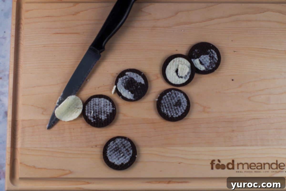 Decadent Dulce De Leche Chocolate Raspberry Icebox Cake 4 Oreo thins being cut in half and filling scraped out on cutting board with knife.