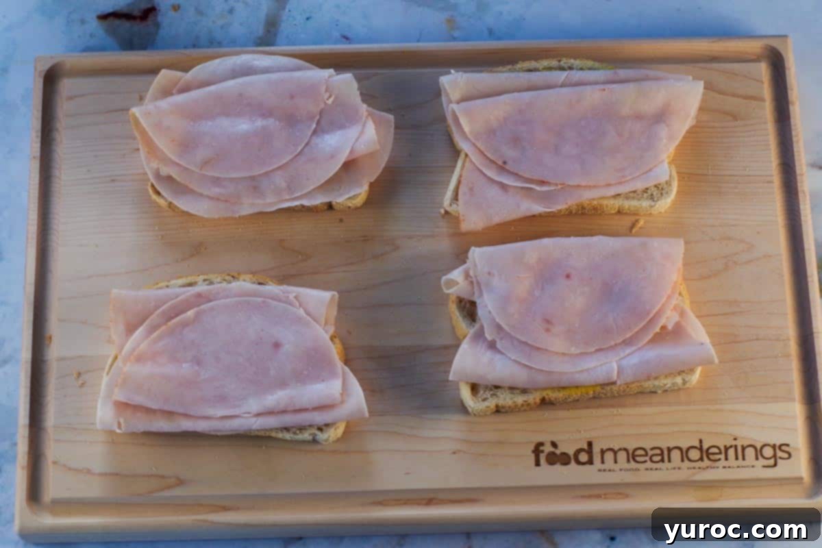 4 pieces of bread with mustard and turkey breast slices on cutting board.