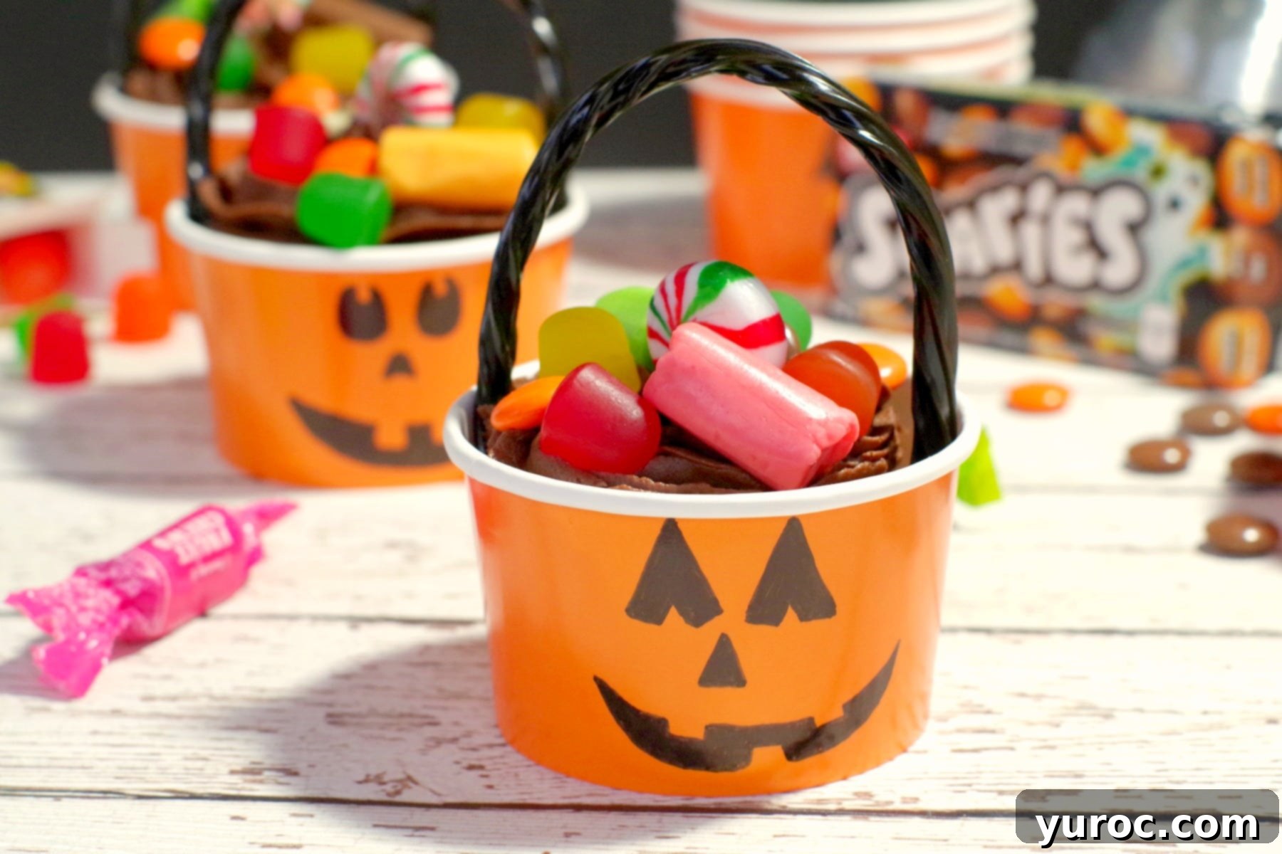 Halloween Jack o'latern bucket cupcake with candy strewn around, highlighting the playful presentation