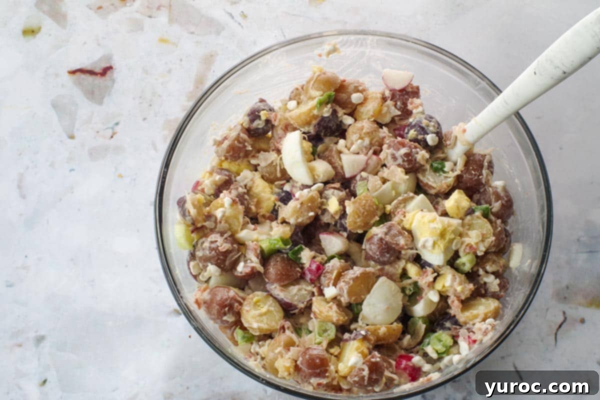 Signature Pierogi Potato Salad 13 Eggs added to potato salad in large glass bowl with marble silicone spoon.
