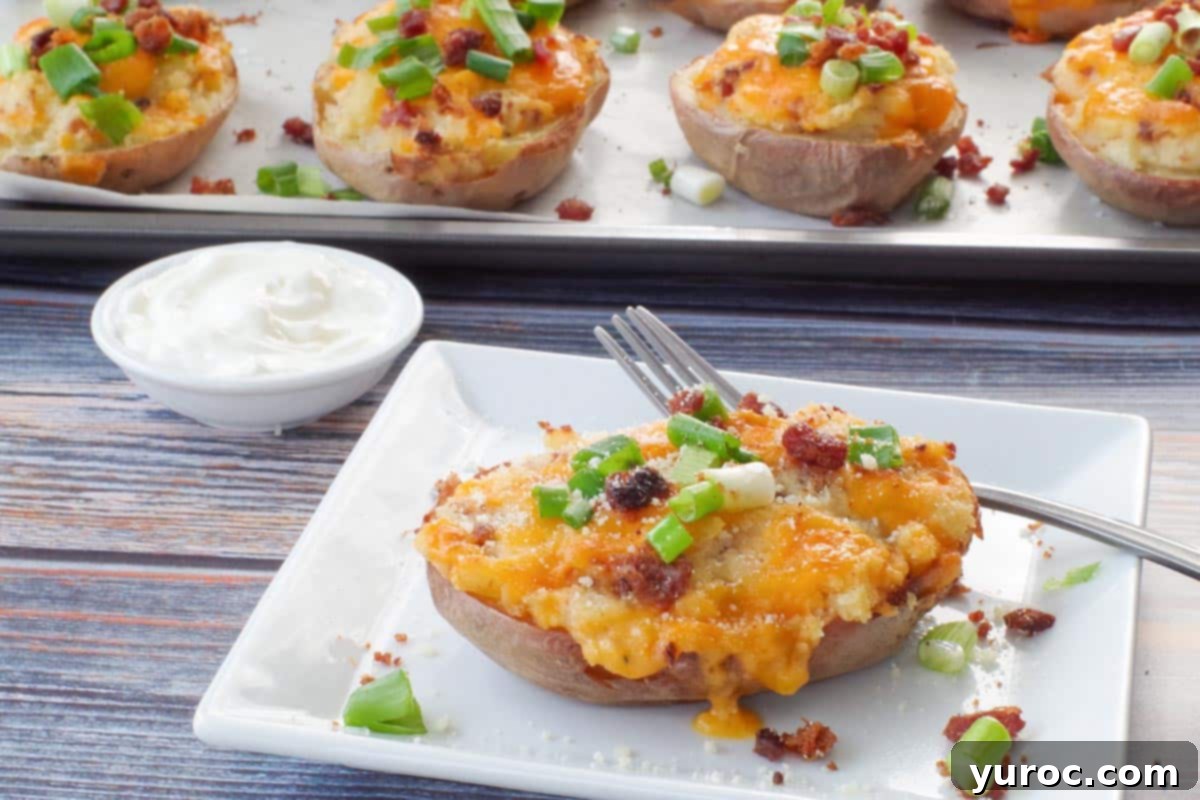 A perfectly golden-brown Caesar twice baked potato resting on a pristine white plate, accompanied by a fork and a small dish of sour cream. In the soft-focus background, a baking sheet holds more freshly prepared potatoes, suggesting a hearty batch.
