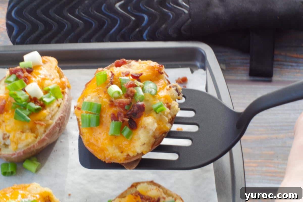 A perfectly stuffed and baked twice baked potato being carefully lifted off a parchment-lined baking sheet with a spatula, highlighting its fluffy texture and golden-brown crust.
