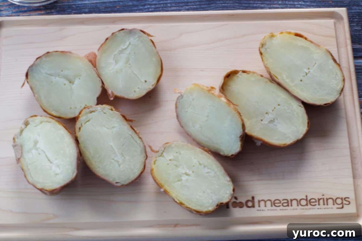 Four baked potatoes, perfectly cooked and cut in half lengthwise, arranged on a rustic wooden cutting board, ready for the next step of preparation.