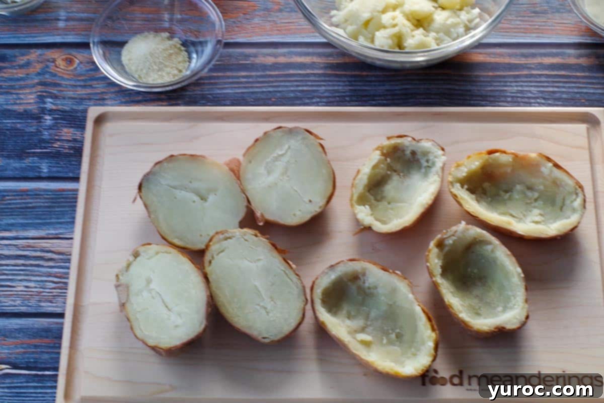 Eight potato halves on a cutting board, with the flesh expertly scooped out of four of them, leaving a thin border inside the skins to maintain their shape.
