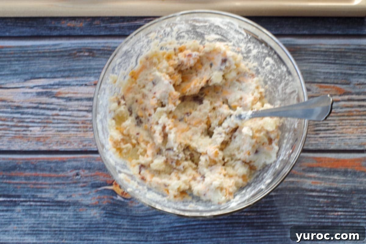 A vibrant and creamy mixture of twice baked Caesar potato filling, enriched with cheese, bacon bits, and chopped green onions, ready in a glass bowl.