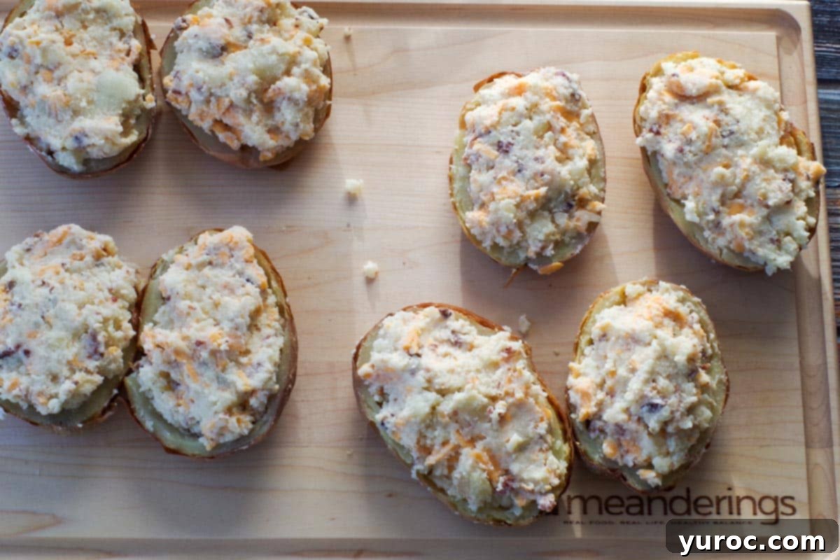 Potato shells generously stuffed with the creamy, cheesy filling, arranged on a wooden cutting board, showcasing the preparation before the final bake.