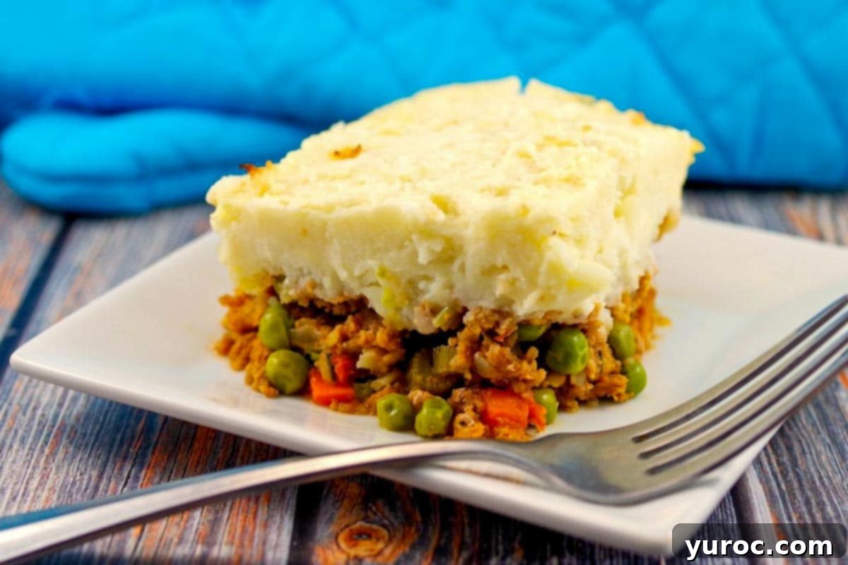 Smart Turkey Shepherd's Pie 2 Ground turkey shepherd's pie on a white plate with a fork and blue oven mitt in the background, showcasing its golden mashed potato topping.