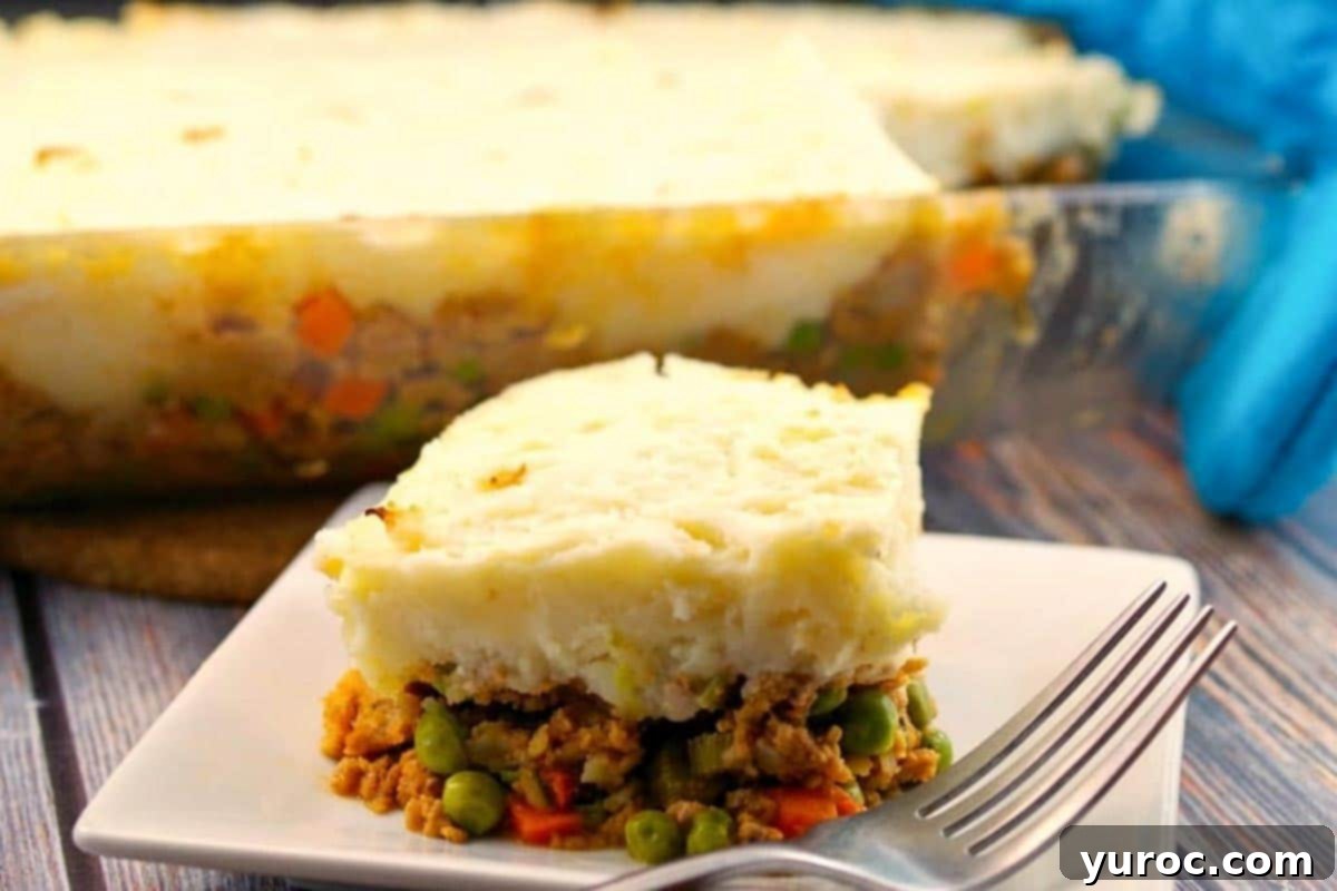 Smart Turkey Shepherd's Pie 13 Ground turkey shepherd's pie on a white plate with a fork, with a larger glass pan of the pie blurred in the background, emphasizing the deliciousness.