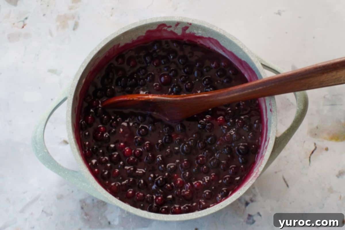 Saskatoon Berry Pie: Mastering the Filling and Sauce 6 Saskatoon berry mixture simmering in a blue pot with wooden spoon.