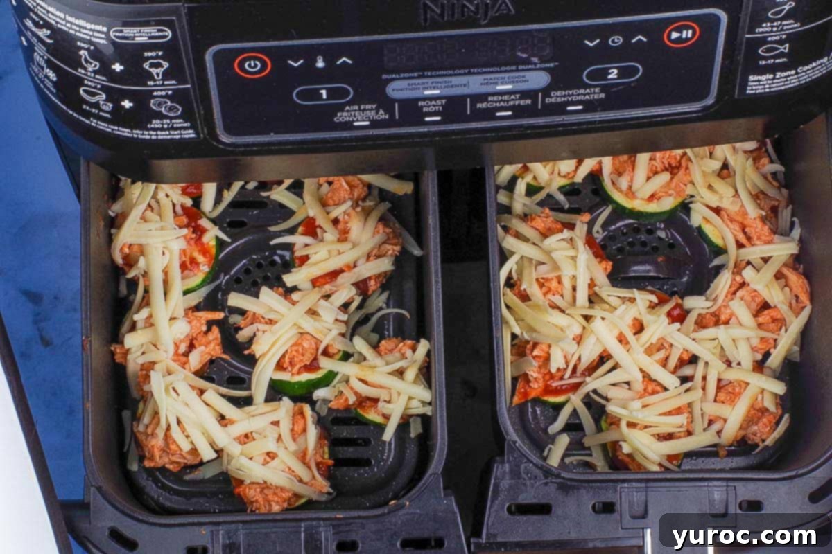 Shredded mozzarella cheese sprinkled over the buffalo chicken and pizza sauce on zucchini bites.