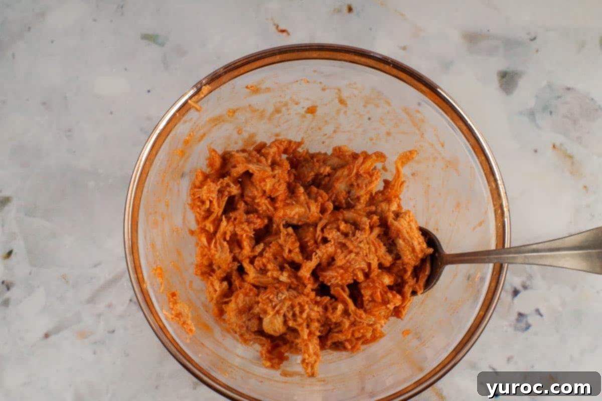 Shredded chicken mixed with buffalo sauce in a bowl, prepared for the pizza bites.