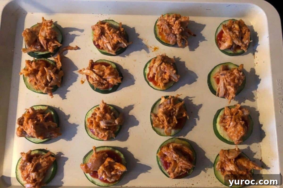 Zucchini bites with pizza sauce and buffalo chicken toppings on a baking sheet.