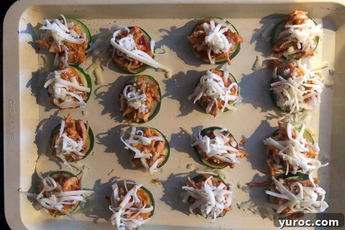 Shredded mozzarella cheese sprinkled over the buffalo chicken and pizza sauce on zucchini bites, ready for the final bake.