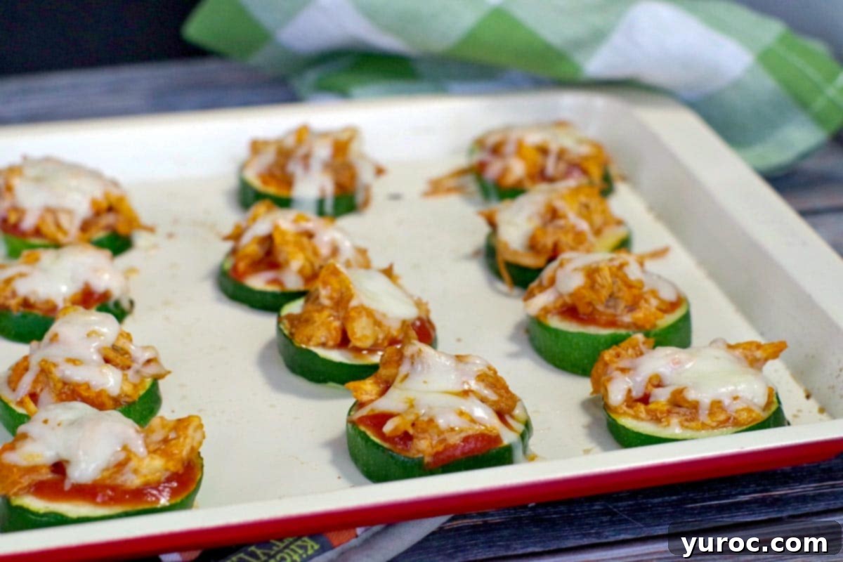 Perfectly baked Buffalo Chicken Zucchini Pizza Bites arranged on an off-white baking tray, hot and ready to serve.