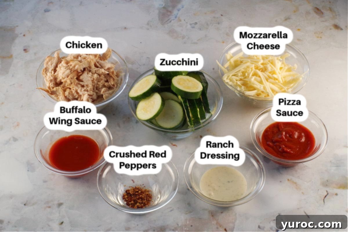 Various ingredients for Buffalo Chicken Zucchini Pizza Bites laid out in glass bowls, including zucchini slices, buffalo sauce, pizza sauce, shredded chicken, mozzarella, and ranch dressing.