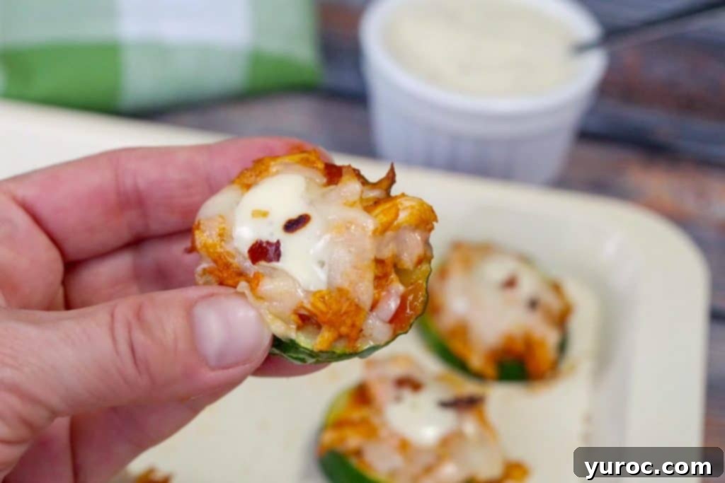 Hand holding a single Buffalo Chicken Zucchini Pizza Bite, highlighting its perfectly baked texture and inviting toppings.