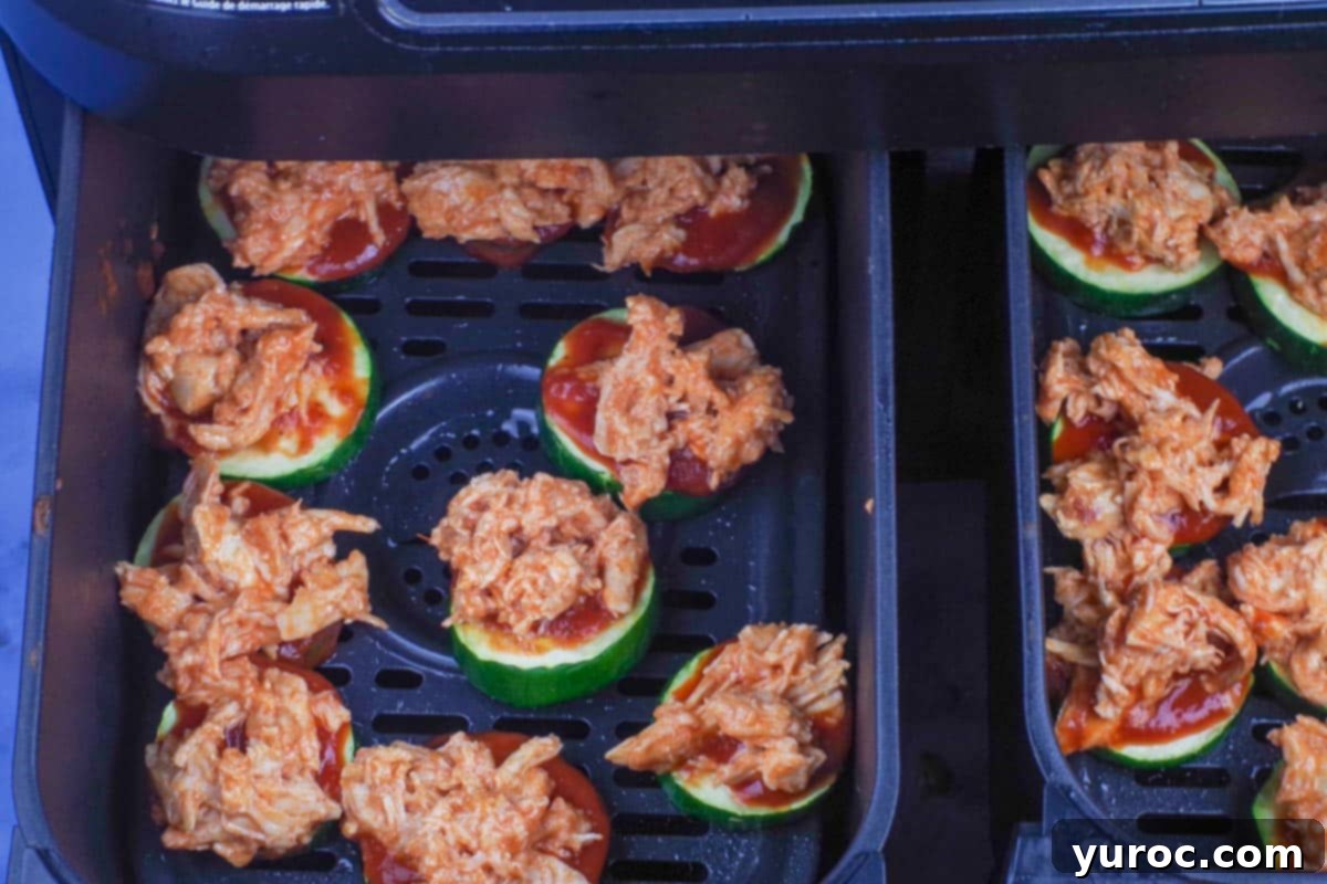 Buffalo chicken mixture generously added on top of the pizza sauce on zucchini slices.