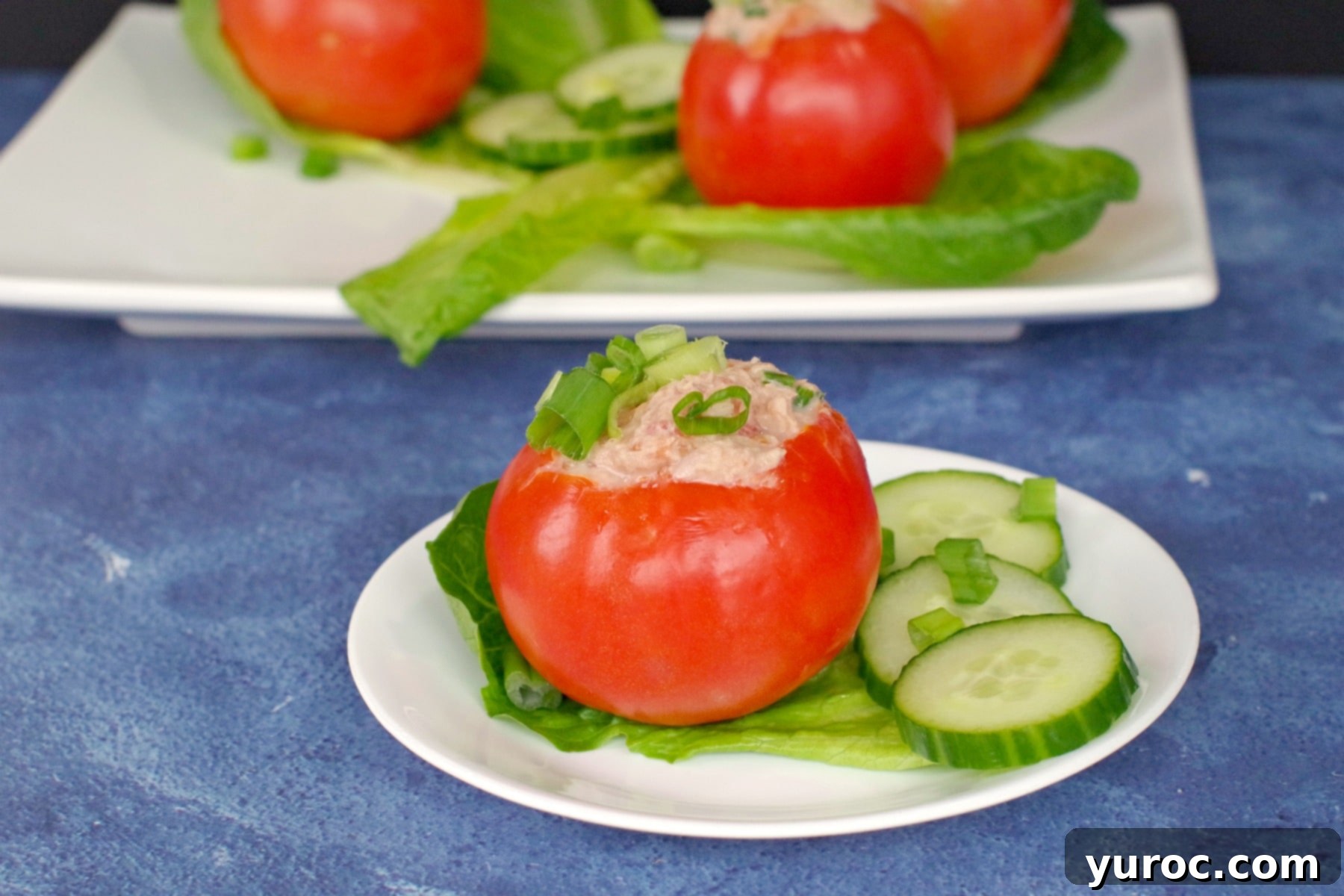 Tuna stuffed tomato on white plate with 3 more tomatoes on platter in background