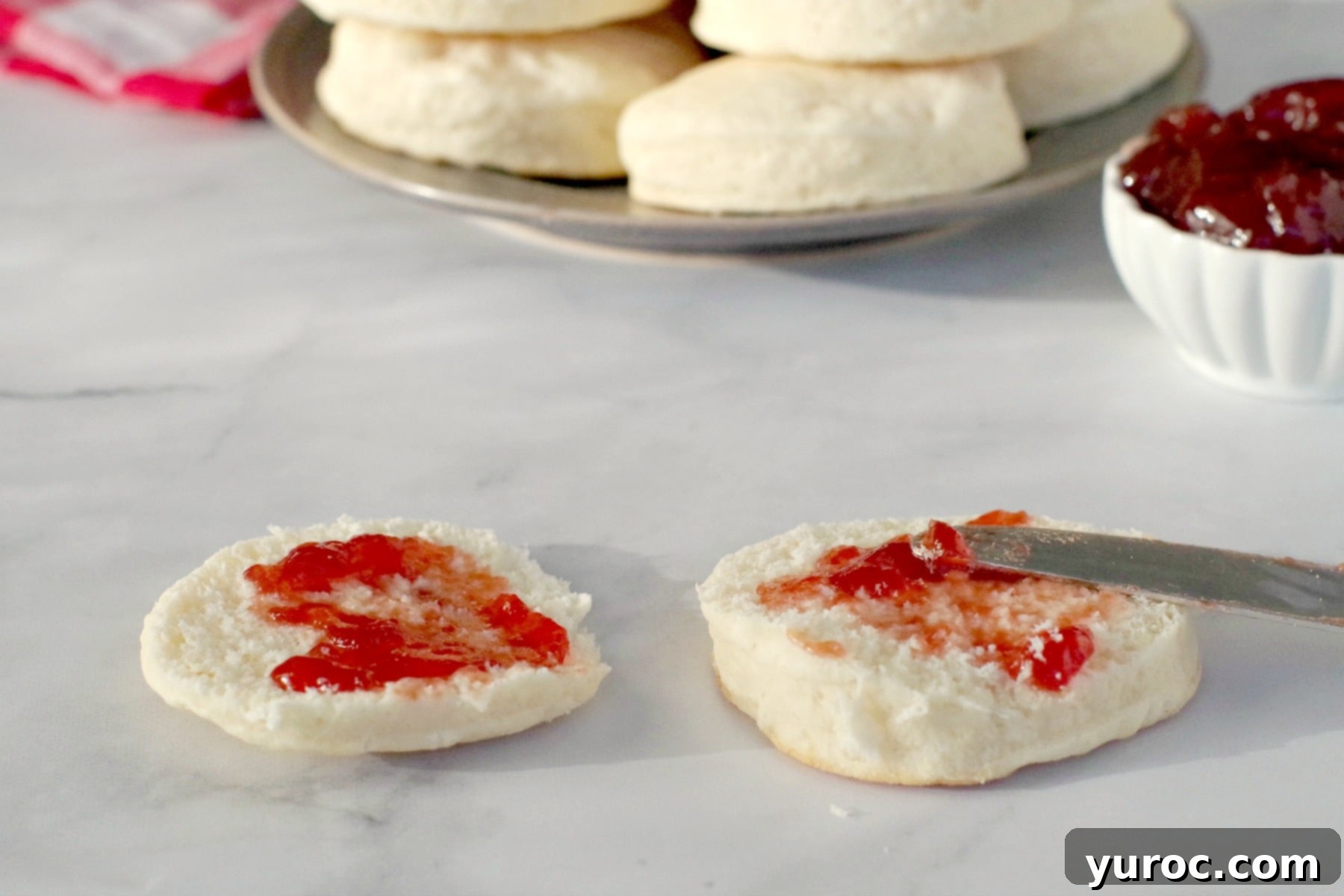 A perfectly baked baking powder biscuit topped with a dollop of sweet raspberry jam, highlighting its golden crust and soft interior.