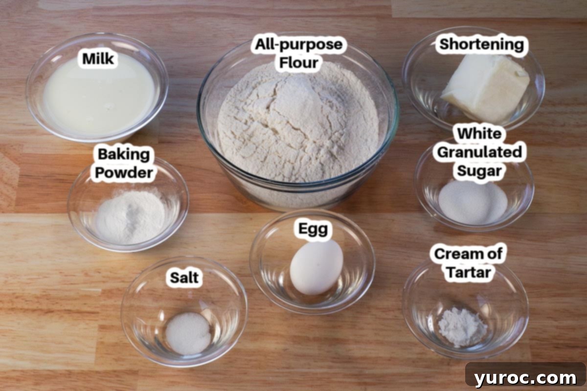 A collection of labeled glass bowls containing the simple ingredients for old-fashioned biscuits: flour, shortening, baking powder, cream of tartar, salt, sugar, egg, and milk.
