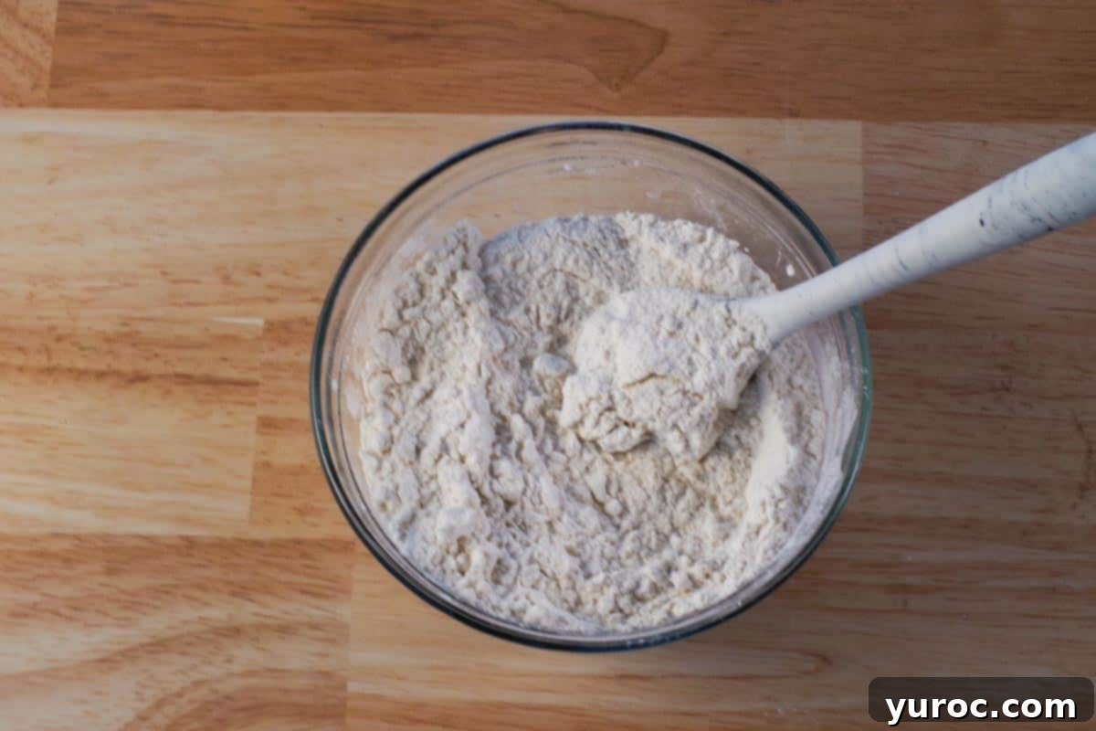 Dry ingredients for old-fashioned baking powder biscuits, including flour, cream of tartar, salt, baking powder, and sugar, mixed together in a large glass bowl with a silicone spoon.