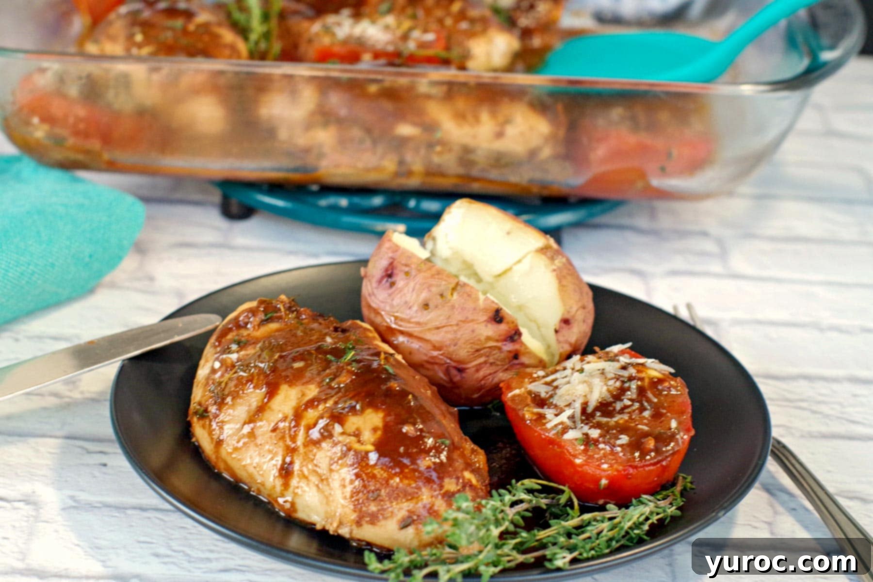 Balsamic chicken and tomatoes with baked potato on a black plate with a glass container of balsamic chicken in background