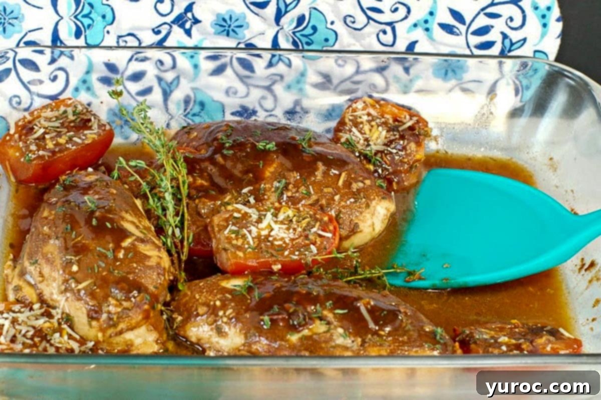 Balsamic chicken with tomatoes in a glass dish with an aqua blue spatula