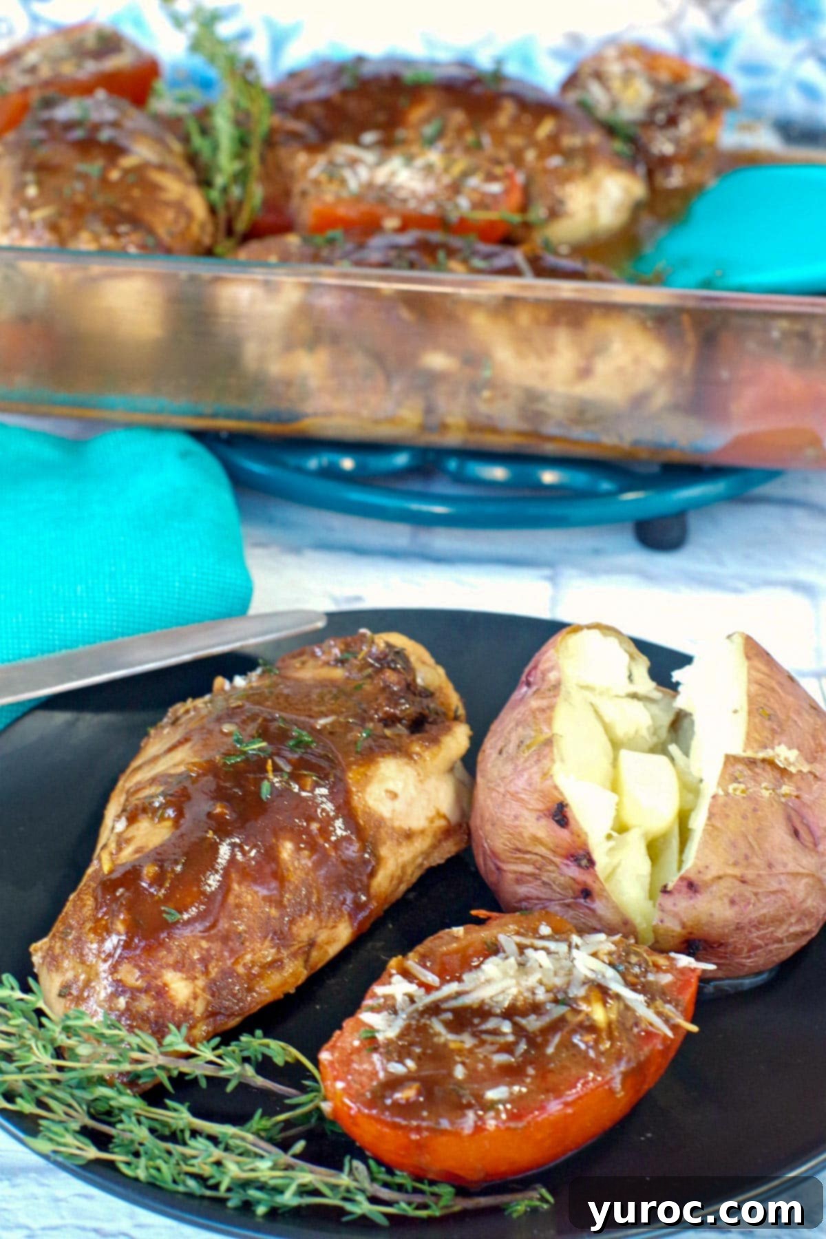 Balsamic chicken and tomatoes with baked potato on a black plate with a glass container of balsamic chicken in background