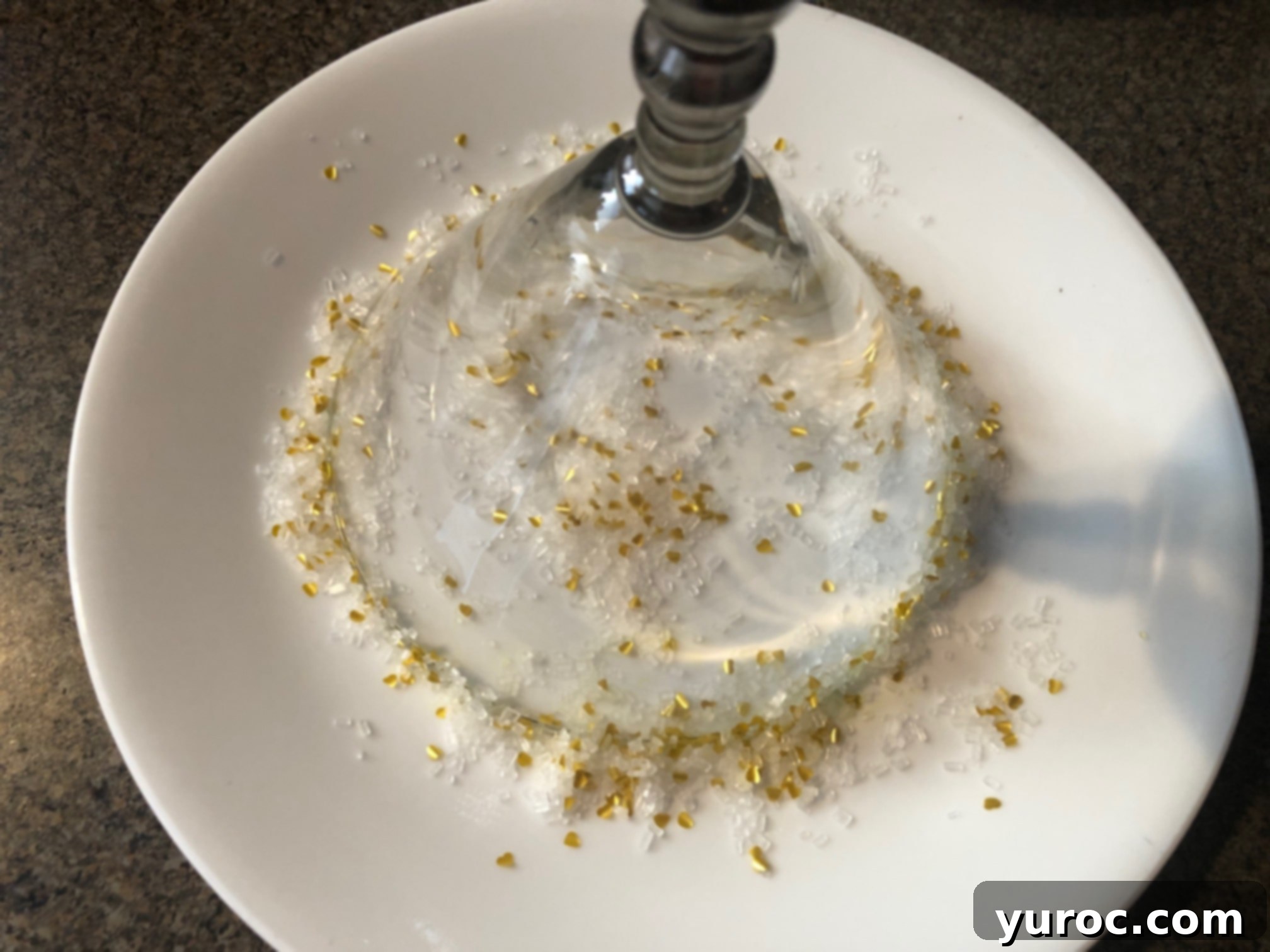 Glass placed upside down on a plate, coating its rim with sparkling sugar and glitter.