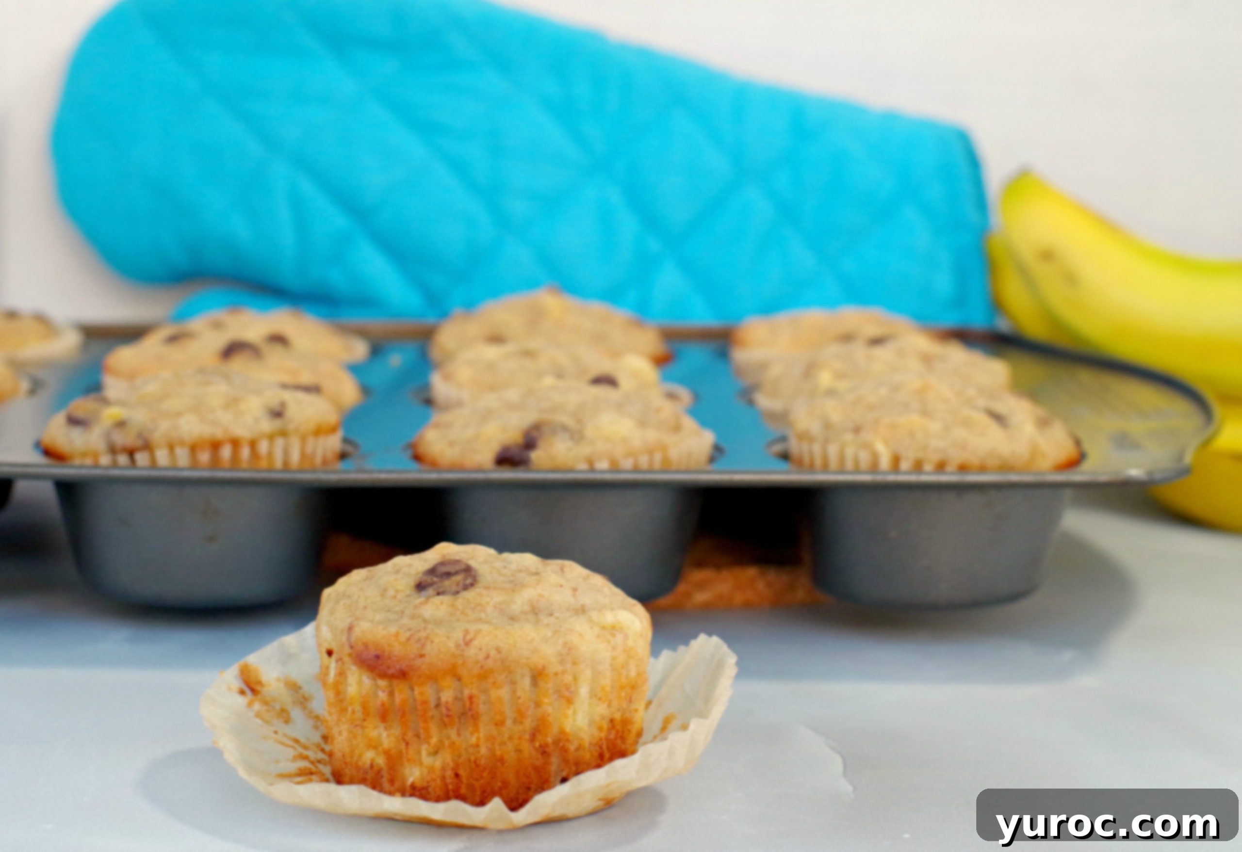 Wholesome Banana Pineapple Chocolate Chip Muffins 2 Healthy Banana Chocolate Chip muffins with pineapple in a muffin tin in background with muffin (with liner off) in front