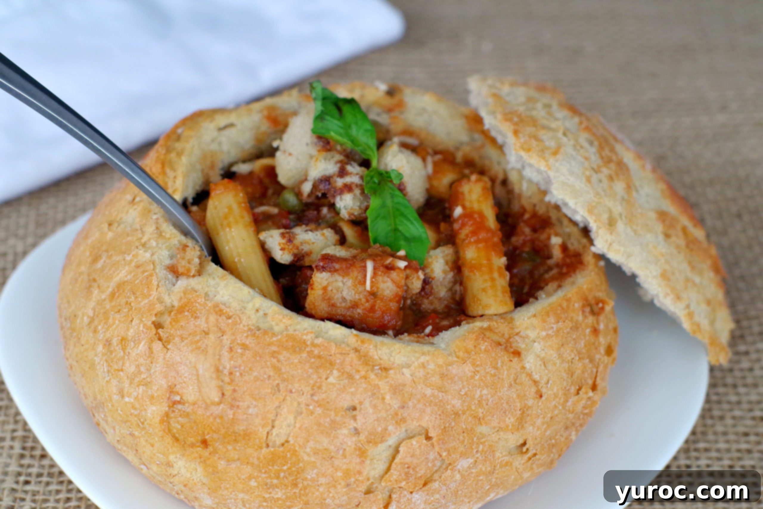 A close-up shot of Panzanella Pasta Soup in a sourdough bread bowl, garnished with fresh basil and a spoon, ready to be enjoyed.