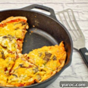 Egg white breakfast pizza in black cast iron frying pan, with piece missing