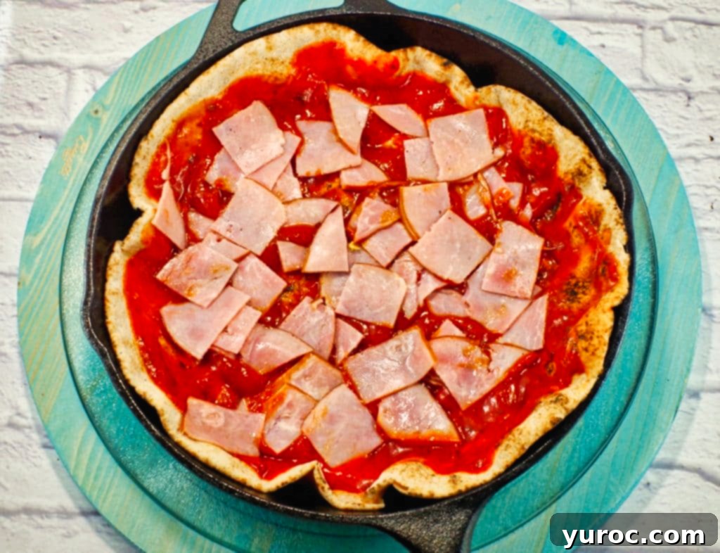 pita bread in a cast iron frying pan with ham and sauce on top
