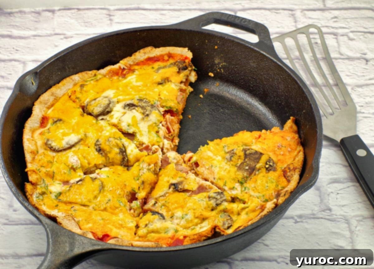 Egg white breakfast pizza in black cast iron frying pan, with piece missing