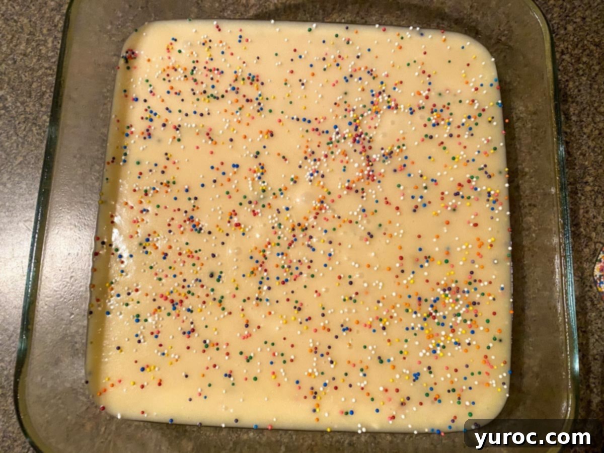 Easy Sugar Cookie Fudge 5 Smooth sugar cookie fudge batter in a glass pan, beautifully adorned with colorful sprinkles scattered across its surface.