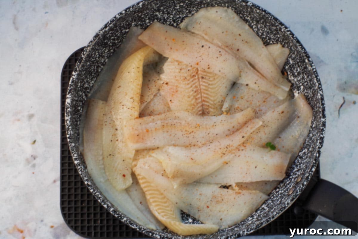 Fish in a frying pan, sprinkled with seasoning.