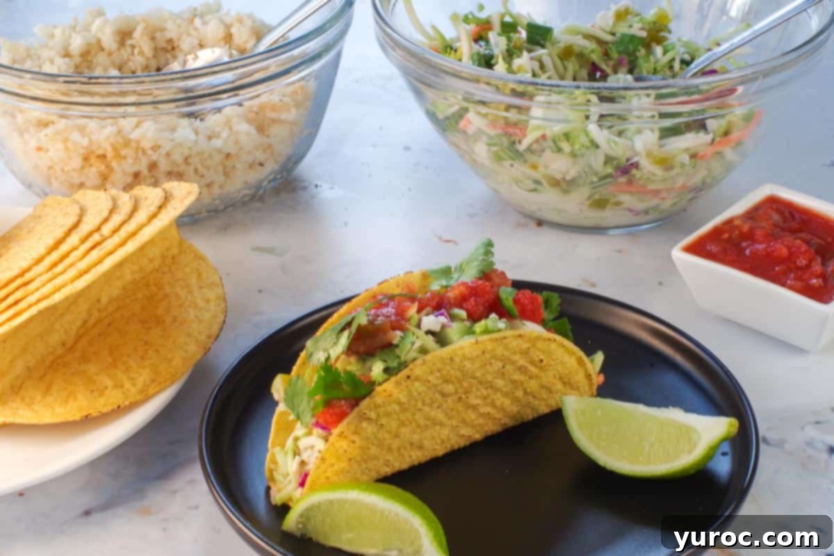 A prepared fish taco on a plate with lime wedges, with all the components (taco shells, fish, broccoli slaw) laid out for assembly.