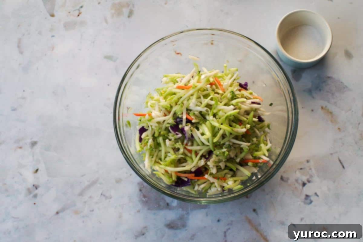 Broccoli slaw mix in a glass bowl with salt sprinkled over it.