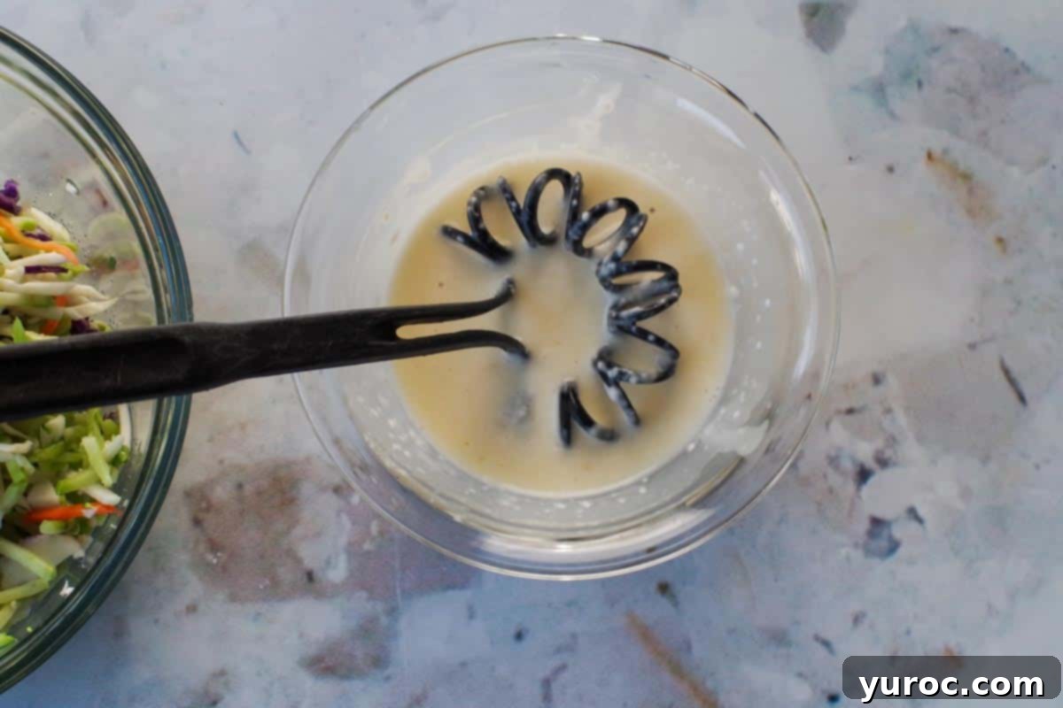 Broccoli slaw dressing ingredients being whisked together in a small glass bowl.