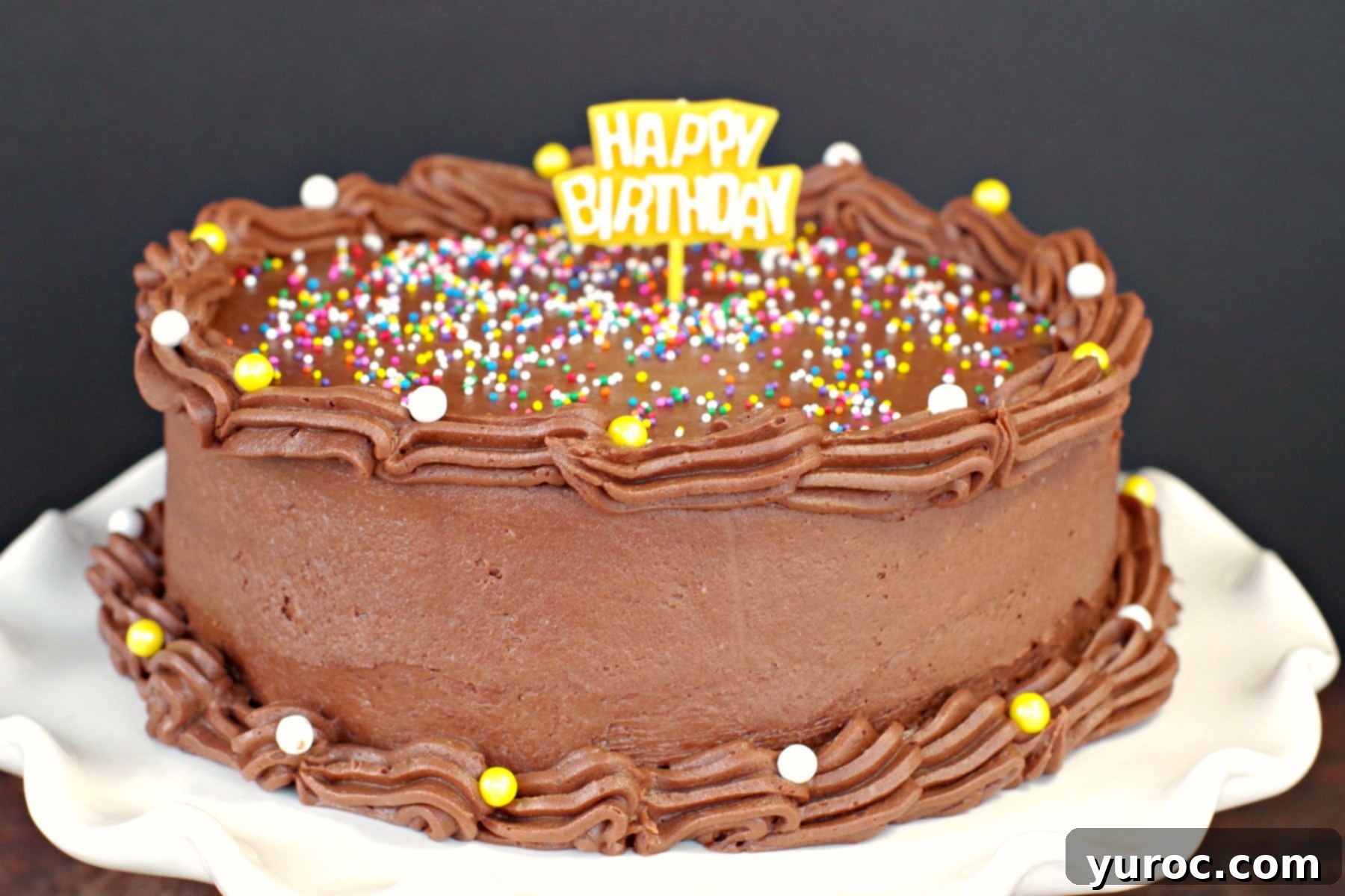 Happy birthday cake decorated with chocolate frosting without butter, adorned with colorful sprinkles and a 'Happy Birthday' topper