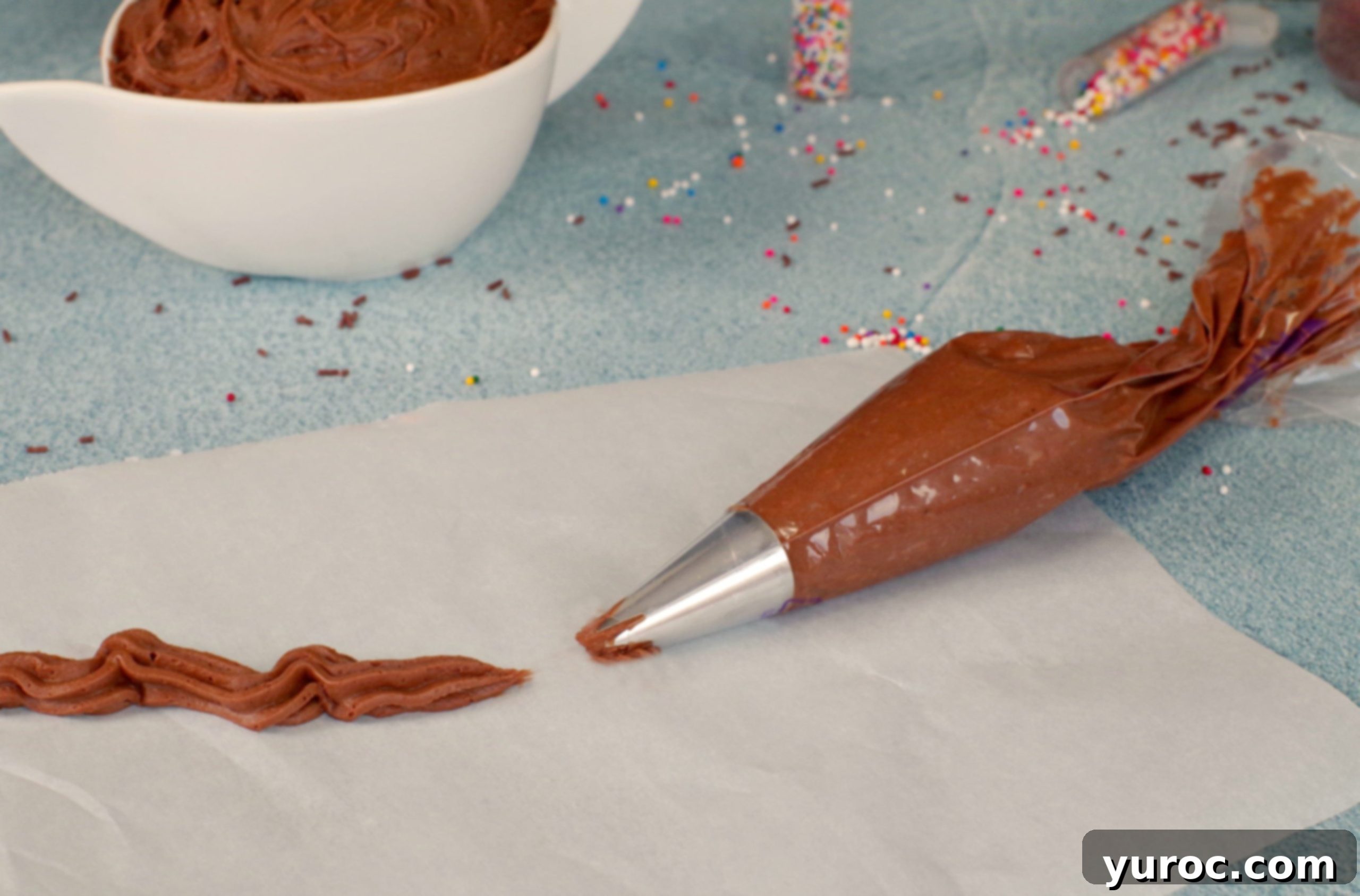 Chocolate frosting in a piping bag with a line of frosting piped onto parchment paper, demonstrating texture