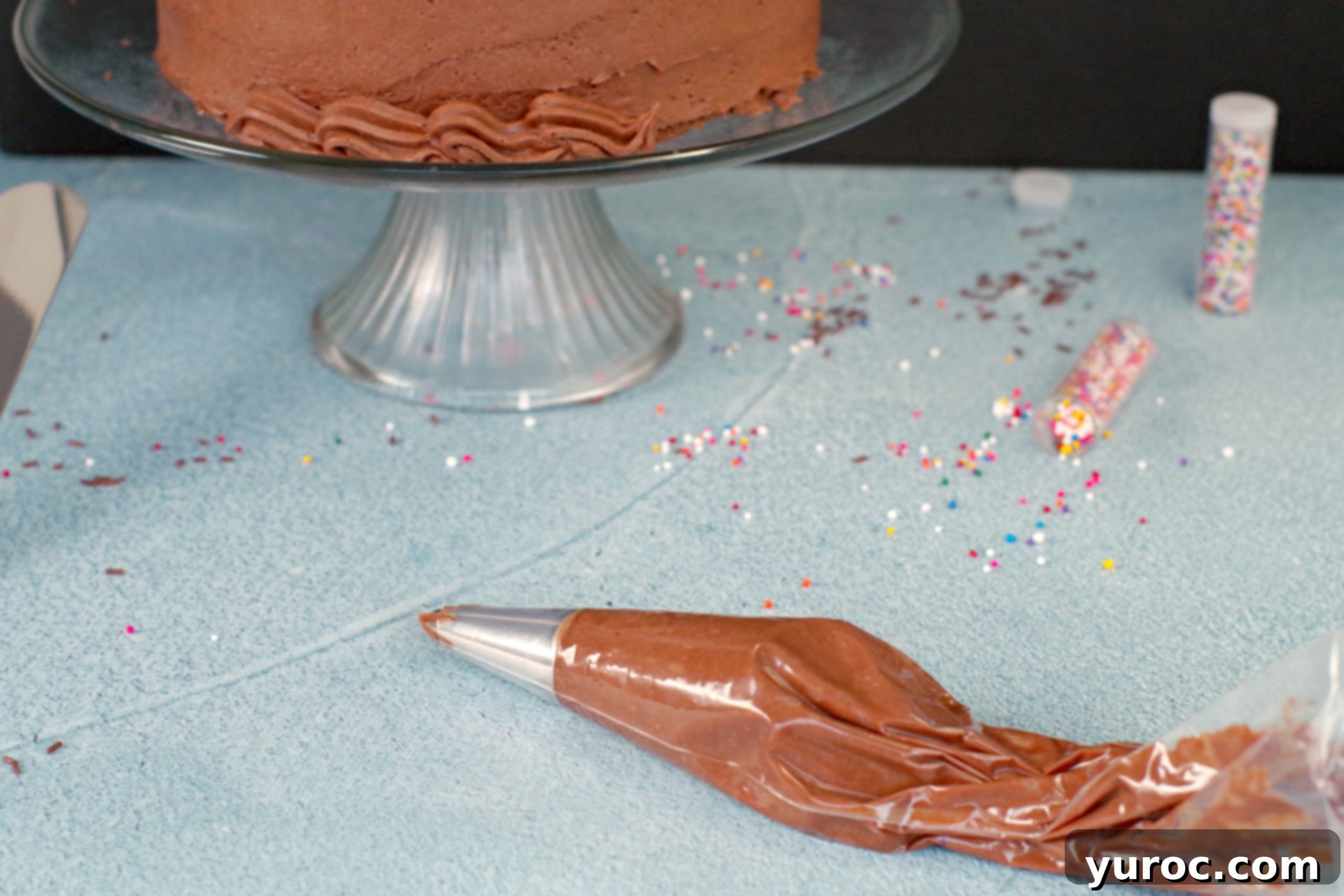 Chocolate frosting in pastry bag with partially decorated cake in the background, showing smooth frosting on the cake surface