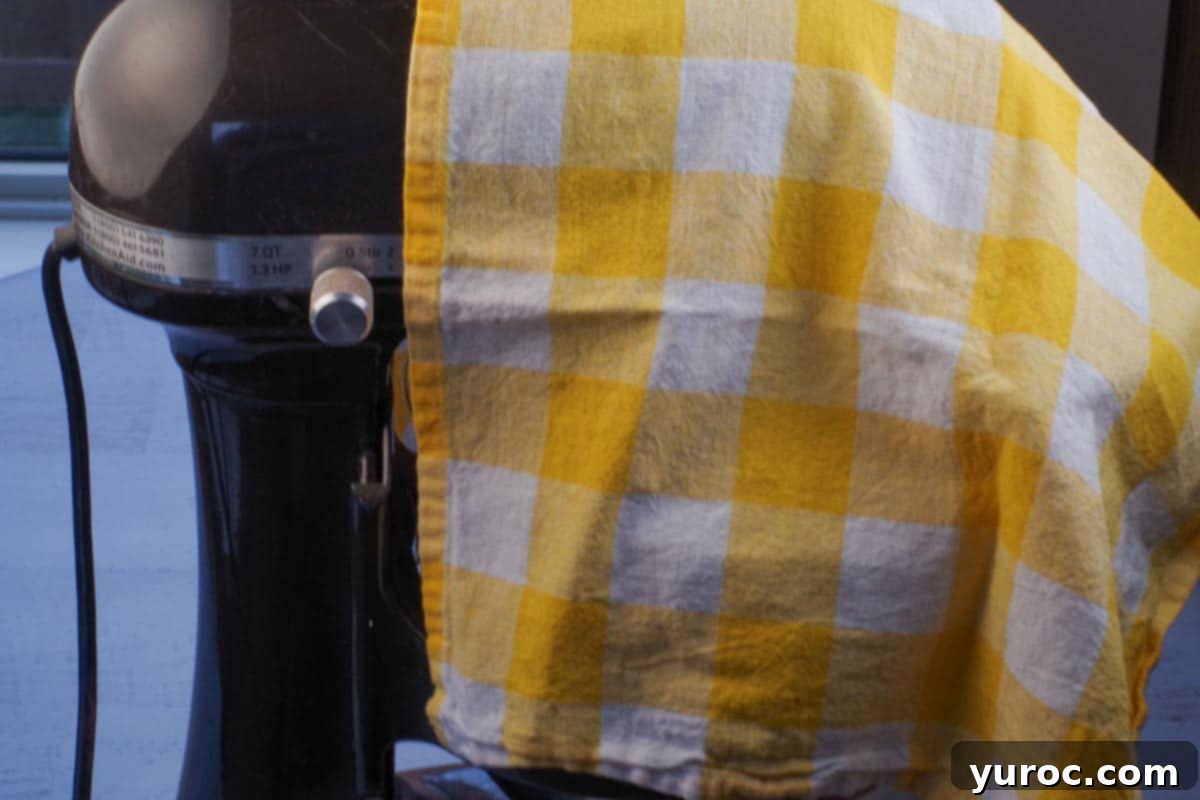 stand mixer covered with a white and yellow checkered tea towel to prevent powder mess
